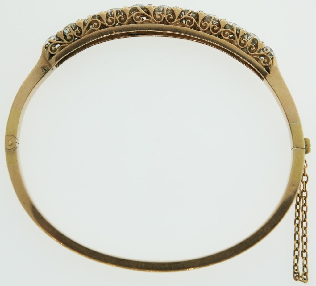 A rose gold 15 karat bangle bracelet with 11 old mine cut diamonds across the top set in ornate scroll work.