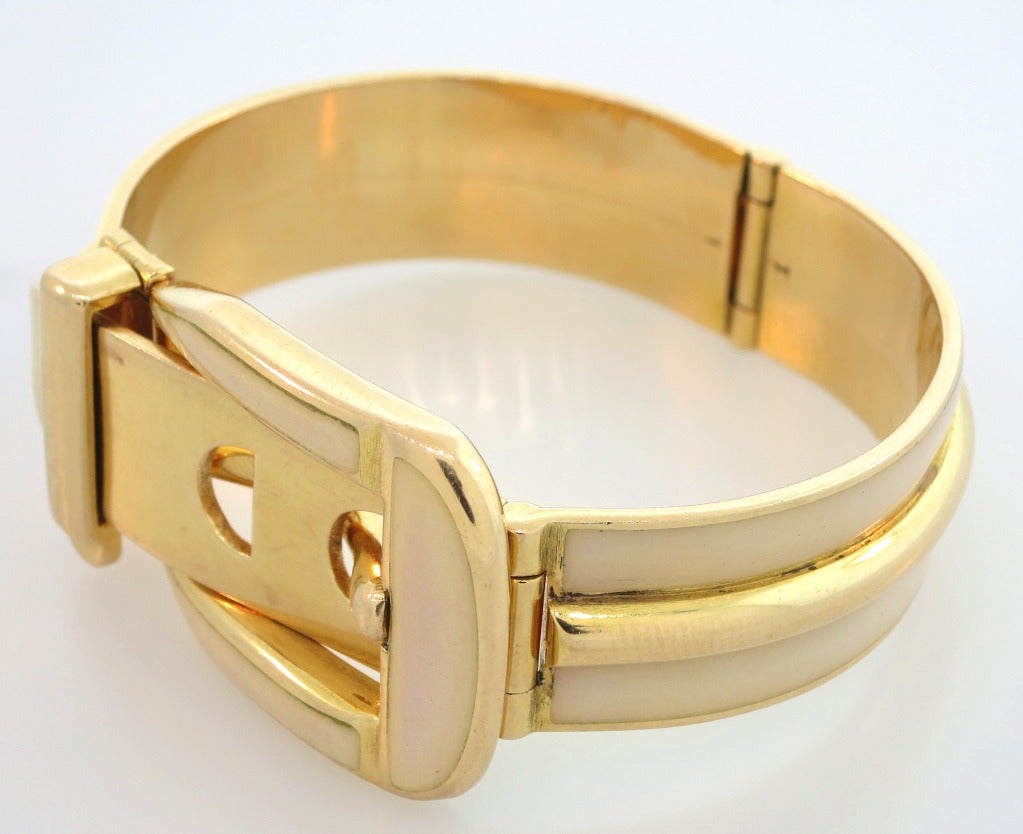 An 18 karat yellow gold hinged bracelet designed as a belt with a buckle, enhanced with cream enamel.