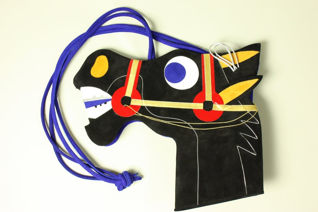 Suede handbag from Andrea Pfister dates to the 1980's.  It depicts a cartoon-like horse head with a golden bit.  Reverse side is royal blue.  Interior is lined with marigold satin.  Snap closure.

Measurements-

Length: 12