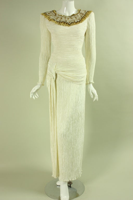 Vintage gown from Mary McFadden dates to the 1980's through early 1990's.  It is made from her signature pleated fabric with a beaded embellishment around the neckline.  Gathered knot detail at side right hip.  Center back and side zip. 