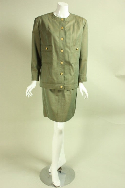 Vintage skirt suit from Chanel dates to the 1980's and is made of green sharkskin cotton.  Single-breasted jacket has patch pockets, round neck, long sleeves with single button cuffs, and gold-toned buttons with iconic interlocking C's.  Straight