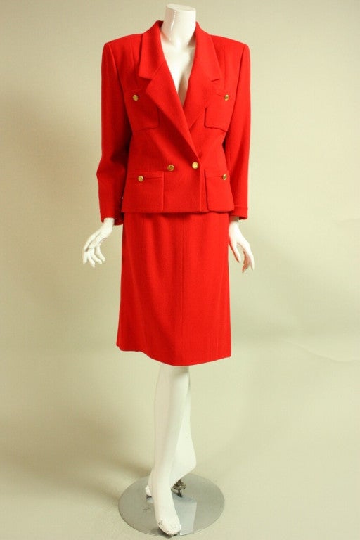 Timeless suit from Chanel dates to the 1980's and is made of bright red wool.  Double-breasted jacket has four patch pockets, long sleeves with buttoned cuffs, and gold-toned buttons featuring portraits of Coco Chanel.  Straight skirt has zippered