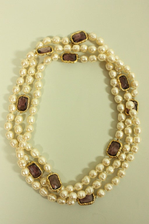 Vintage sautoir necklace from Chanel dates to 1981 and is made of cream-colored faux pearls and faceted purple gripoix beads.  The beads are encased in gold-toned metal and spaced at irregular intervals.  No closure.  Measures 62