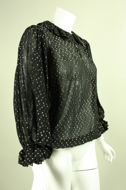 Vintage blouse from YSL dates to the 1970's and is made of black silk chiffon with metallic gold polkadots.  Keyhole neckline with gathered ruffle detail around the neck.  3/4-length sleeves with ruffled cuffs.  Unlined.  Center front hook and eye