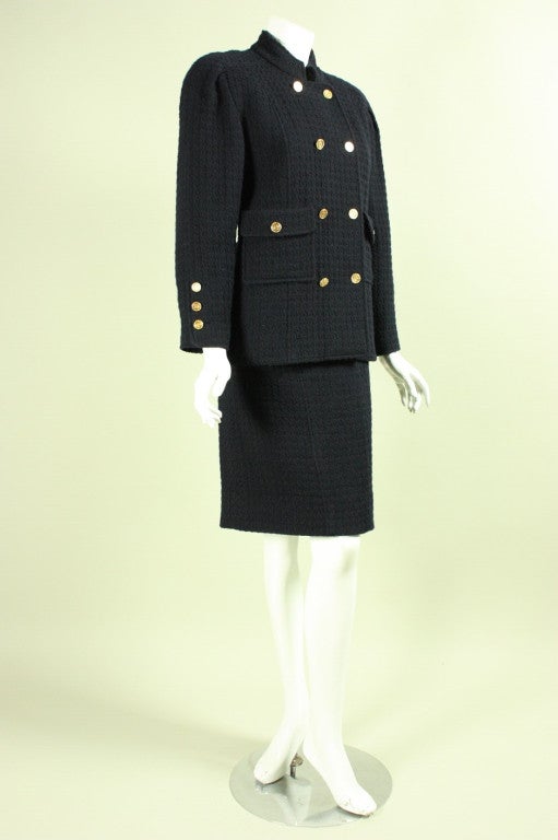 Vintage suit from Chanel dates to the 1980's and is made of navy wool bouclé.  Boxy jacket has stand collar, is double breasted, and features gold toned metal buttons.  Straight skirt has zippered closure.  Both pieces are lined.  Both are labeled