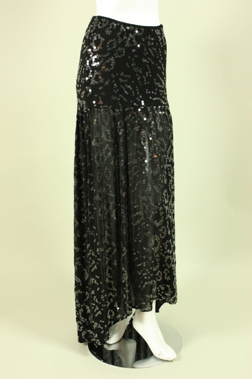 1990’s skirt by Ghost is made of a black viscose blend fabric that is entirely covered with clear sequins.  It is fitted from the waist to the hip and then is gathered all around the seam at the hip to create fullness.  It is longer in the back than