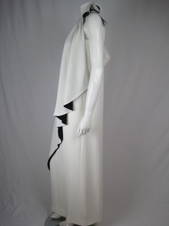 Stunning one-shouldered evening gown with flounce detail.  Separate piece of off-white crepe backed with black crepe  attaches at left side seam and drapes diagonally down front. Gathering at right shoulder.  Right side zip.  Fully lined.<br />
<br