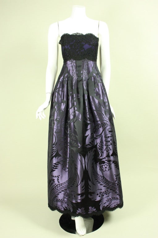Gorgeous gown and evening jacket from Geoffrey Beene dates to the 1990's.  Strapless dress has a black lace bodice with scalloped edges, purple and black jacquard skirt with volume formed by darts throughout the waistline, and a scalloped lace hem. 
