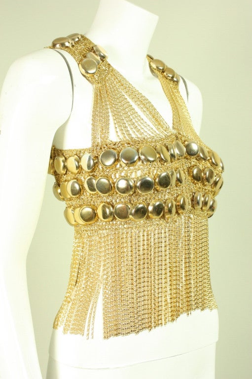 Glam vest from French designer Loris Azzaro is made of metallic gold knit fabric that is joined together by rows of gold-toned metal chain link.  Knit areas are covered with three-dimensional metal discs.  Center front triple snap closure.  Unlined.