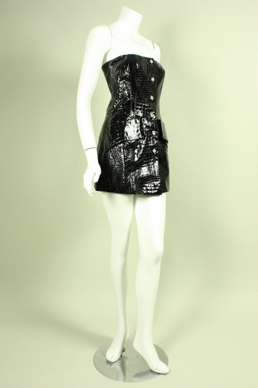 Mini dress from James Galanos retailed at Neiman Marcus and dates to the latter part of his career likely between the 1980's through the 1990's.  It is made of jet black, crocodile-embossed vinyl with clear faceted rhinestone buttons.  Slanted hip