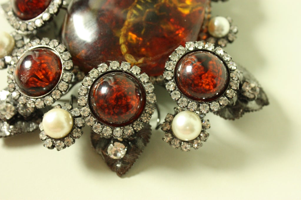 Oversized brooch from Lawrence Vrba has an amber resin center with a scorpion inside.  Rhinestone and pearl details.  Gunmetal silver-toned metal.

Width: 4 1/2
