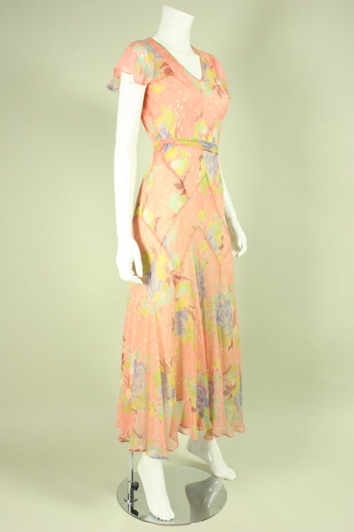 Vintage dress dates to the 1930's and is made of pink silk chiffon with a multicolored pastel floral print.  It has a v-neck, flounce short sleeves, and is cut on the bias.  Separate waist tie can be tied in the front or back.  Lined.  Side snap
