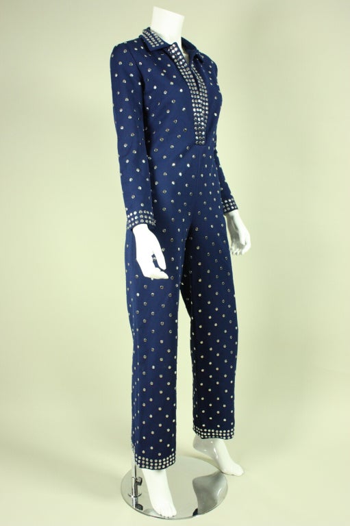 Sassy jumpsuit from Donald Brooks dates to the 1970's and is made of navy synthetic fabric with flat silver metal studs throughout.  Deep v-neck can be made more modest with a hook and eye that is located halfway between the neck opening and the