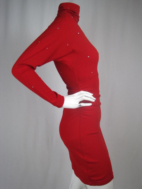 Red knit body conscious dress.  Rhinestone accents throughout the front and back bust as well as down the sleeves.  Shirring at side and back seams creates gathering through the waist and hip.  High turtleneck has shirring at the center back. 