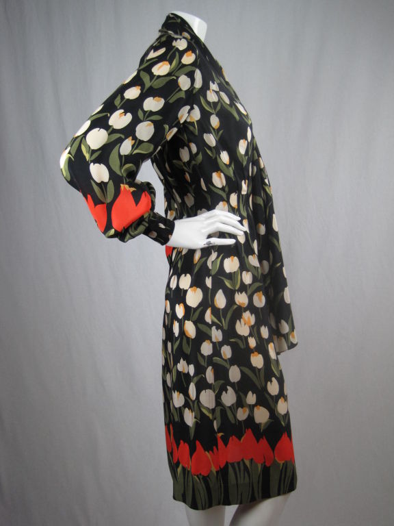 Bill Blass cocktail dress with striking print.  A field of white tulips with yellow centers is accented by large bright orange and green-stemmed tulips that seem to grow out of the hem and cuffs.  Deep v-neck.  Attached scarf is sewn to the dress at