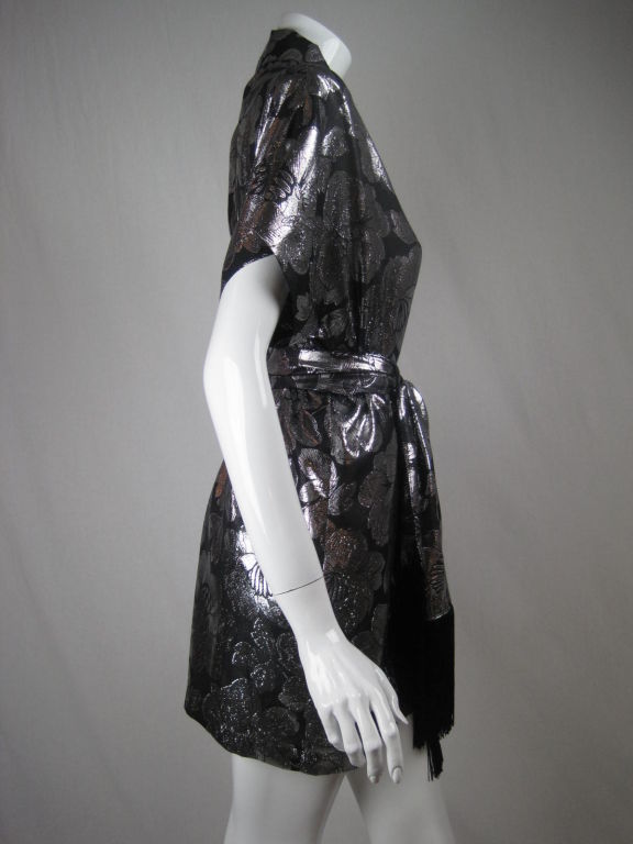 Lovely scarf and matching dress/tunic from the fantastic 1980's label, Genny.  Black and silver lamé with large, allover floral print.  Short sleeves.  Cowl v-neck.  Shoulder pads. Unlined.  Matching scarf is edged with black fringe.<br />
<br