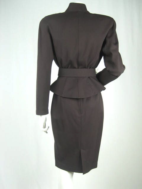 Brown wool skirt suit by Thierry Mugler. Extremely fitted double-breasted jacket with stand up collar, pointed lapels, thick shoulder pads, and flared peplum. Straight high-waisted skirt has back vent and center back zipper. Belt has large silver