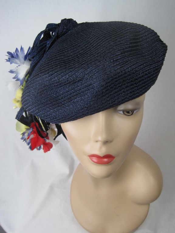 Navy straw beret.  Strips of narrow straw extend out from cap and are punctuated with playful flowers of various colors.  Interior turquoise grosgrain band.  <br />
<br />
Labeled size 22.