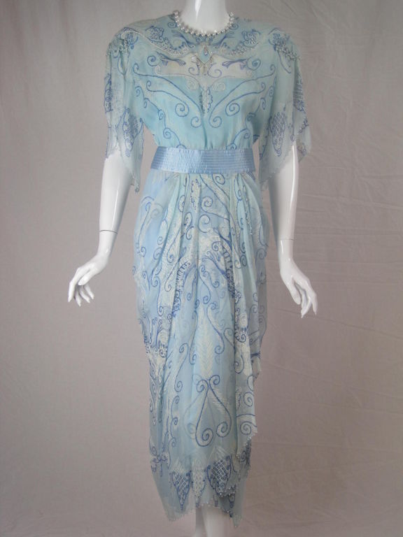Zandra Rhodes tea-length dress.  Light blue silk chiffon with hand silk-screened print.  Transparent cut-out at bust with rhinestone and iridescent beaded details.  Handkerchief sleeves.  Pearls sewn at all edges.  Satin waistband.  Round neck. 