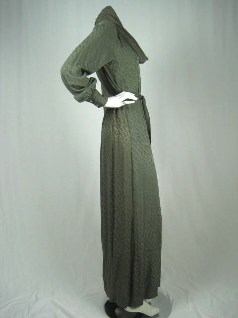 Stunning gown made out of sage green damask silk woven into a diagonal floral pattern. Cowl neck. Voluminous sleeves punctuated at wrists with a double button cuff. Back yoke with gathering below. Can be worn with or without belt. No closures. Circa