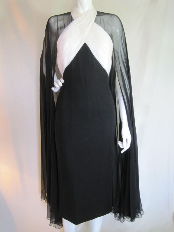 From famed English designer, Murray Arbeid, is this elegant dress made from black and white silk chiffon with an attached cape that covers the shoulders and falls to the hem of the dress. It is fully lined, sleeveless, zips up the center back, has a