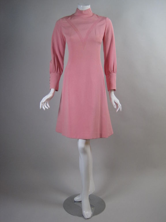 1960's dress designed by James Galanos for the Beverly Hills boutique, Amelia Gray.  Made out of pink silk crepe with machine embroidered "V" on the bodice.  Mock neck.  Long sleeves with button cuffs.  Full skirt is created by side and