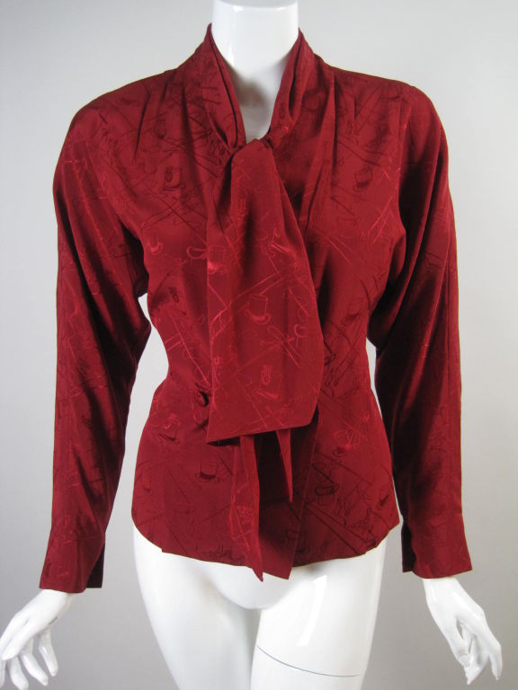 Hermes blouse made out of wine-colored silk jacquard with unusual top hat and crosshatched pattern.  Wrap front with covered button closure at waist.  Attached necktie.  Tapered dolman sleeve with button cuff.  Unlined.<br />
<br />
Labeled size