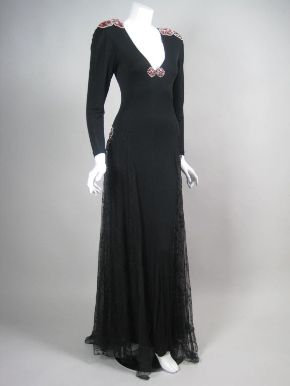 Dramatic 1970's gown from Los Angeles designer, Holly's Harp.  Matte black jersey is adorned with beaded and sequined appliques.  Three panels of embroidered lace fall from the hips and lower back.  Plunging v-neck.  Tapered sleeves.  Padded