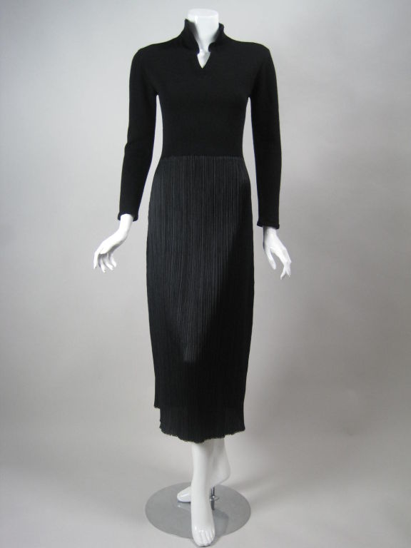 Minimalist sweater dress from Issey Miyake.  Bodice is made of black wool that is finely knit and is connected to the skirt by weaving the yarn through small holes in the skirt's waistline.  V-neck with stand collar.  Straight skirt is pleated and