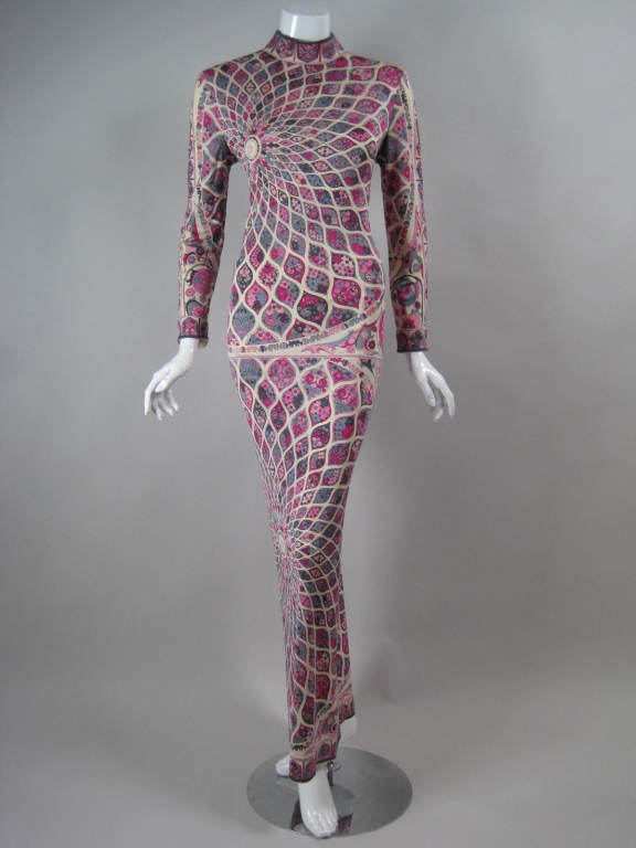 Slinky 1970's gown from Emilio Pucci.  Silk jersey with radiating geometric print in pink, fuchsia, gray, and white.  Drop waist.  Mock neck.  Long tapered sleeves.  Floor-length.  Center back zipper.  Unlined.

Labeled size