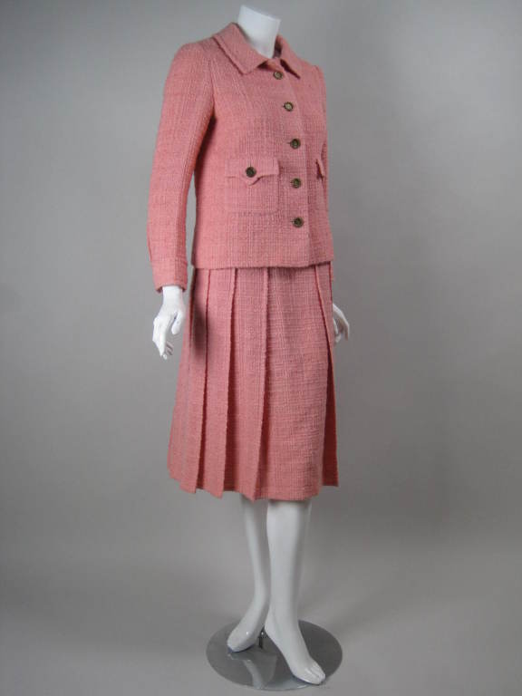 1960's classic Chanel Haute Couture skirt suit is made out of pink wool boucle.  Single-breasted jacket has five button closure, turn down collar, two patch pockets, double button cuffs, and gold chain on interior hem.  Pleated skirt has flat front