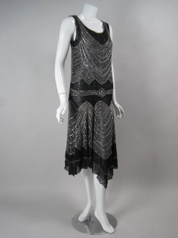 This 1920's dress is a magnificent example of Art Deco wearable textile art.  Fine black cotton fabric has allover adornment of black and silver sequins and glass beads.  Black beads are sewn on in a rhythmic organic pattern while the silver beads