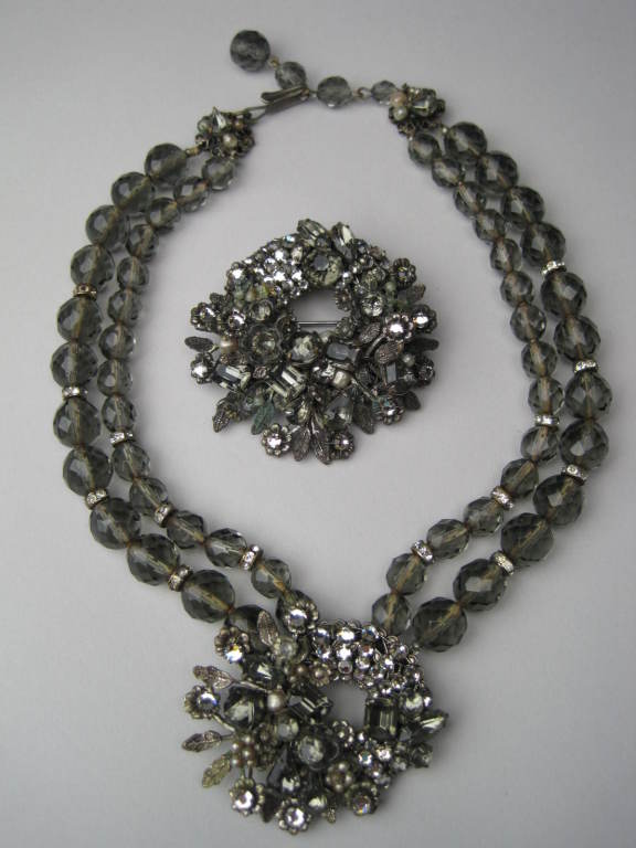 Necklace and brooch set from Robert DeMario is made of silver-toned metal and set with overlapping rhinestones and pearls.  Necklace is made of smokey faceted glass beads with bands of rhinestones separating the beads at regular