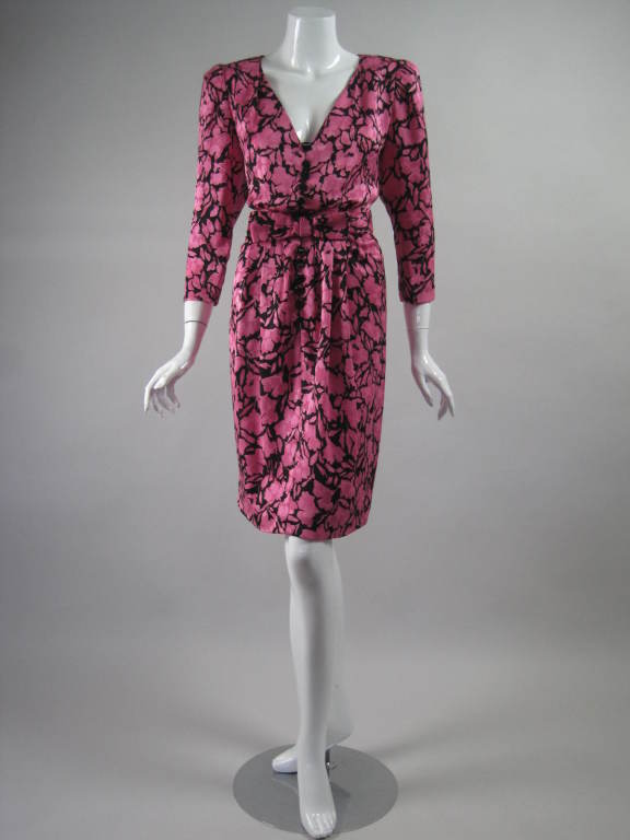 Fun and flirty cocktail dress from Oscar De La Renta is made out of fuchsia and black silk jacquard with a floral print.  Blouson bodice has deep v-neck and 3/4-length sleeves.  Skirt is straight and gathered all around waist.  Faceted black button