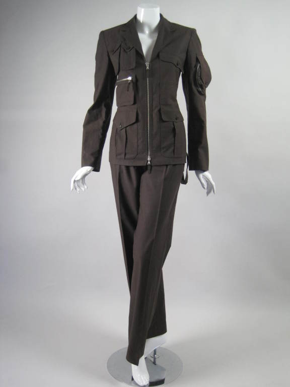 Military-inspired trouser suit from Jean Paul Gaultier is made out of brown cotton.  Blazer has zip front, notch lapel, buckle back, and various utilitarian pockets.  Flat front pants have zip fly and tab closure.  Both pieces are