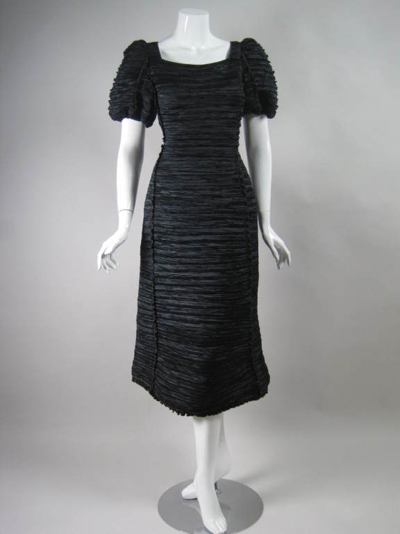 Sculptural cocktail dress from Mary McFadden is made out of black pleated polyester.  Narrow ruffle detail throughout has gold-trimmed edges.  Squared neckline.  Short puffy sleeves with elasticized cuffs.  Side zipper.  Lined.

No size