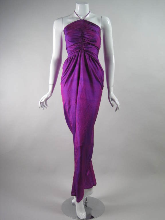 Fabulous 1970's jumpsuit was made by Bill Tice and retailed at Neiman Marcus.  It is made out of purple and magenta two-toned silk shantung.  Fitted bodice has a gathered center front from which halter-style ties emerge.  Pants have gathered