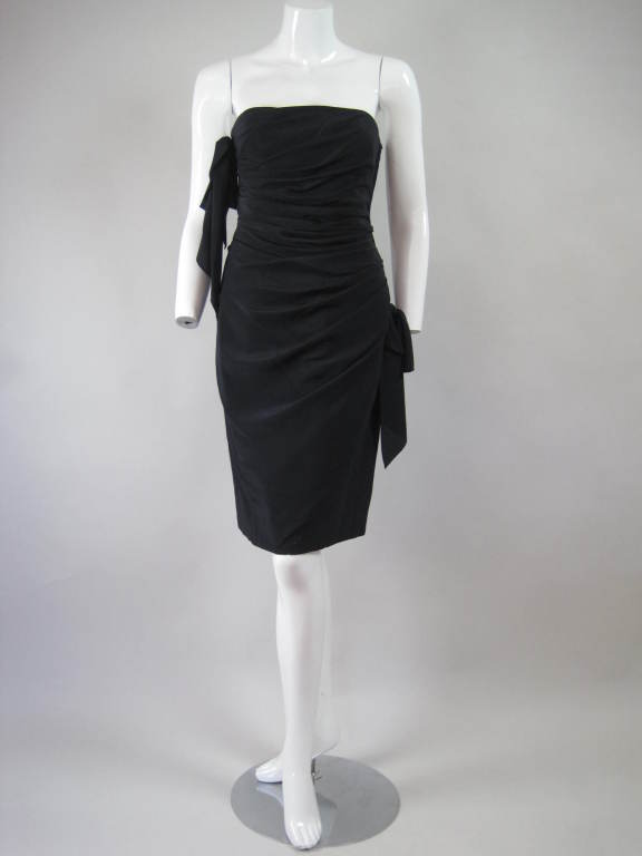 Striking cocktail dress from Emanuel Ungaro is made out of black silk dupioni. It is strapless and has bow details at left hip and right bust.  Flattering side ruching.  Side zip.  Fully lined.

Labeled size 8.

Bust: 34-35
