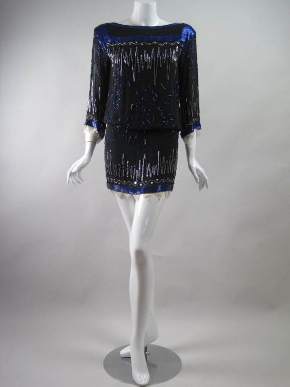 1980's Fabrice dress is made of black silk chiffon with allover beading.  Royal blue and silver glass bugle beads are sewn in irregular zigzagged and swirl patterns. Bands of silver metallic beaded stripes trim the dress at neck and hem. Elasticized