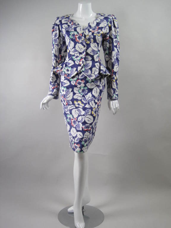 1980's two-piece summer suit from Emanuel Ungaro is made out of dark blue linen with a white and multicolored floral print.  Single-breasted jacket has sweetheart neckline, ruffled peplum, button front, and structured shoulders.  Pencil skirt has