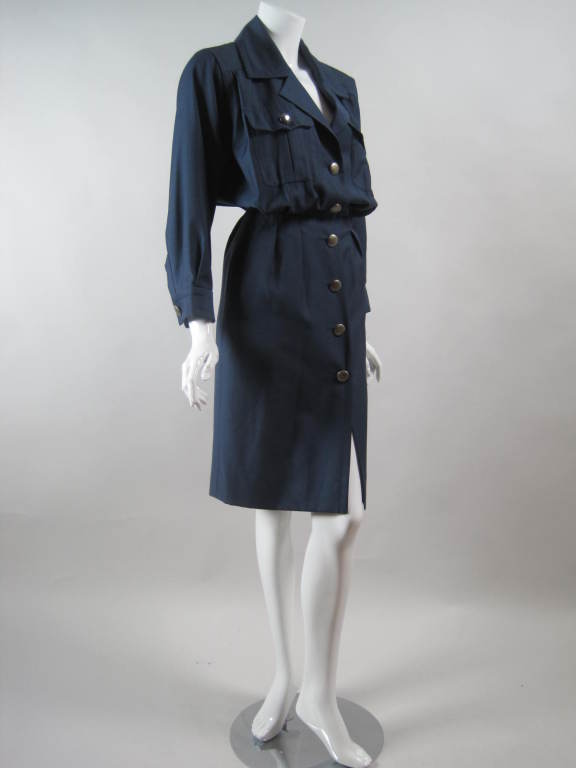 1980's dress from Yves Saint Laurent is made out of lightweight navy wool gabardine.  It has military-styling, which includes a notch lapel, patch pockets at bust with flap closure, and large gunmetal gray metal buttons down the center front.  Long