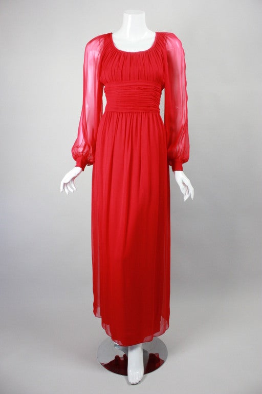 Show-stopping gown from Jean Louis is made out of fire engine red silk chiffon.  Fitted bodice has ruching that emanates from scoop neck.  Wide waistband extends from just under the bust to below the waistline and is highly gathered.  Straight skirt