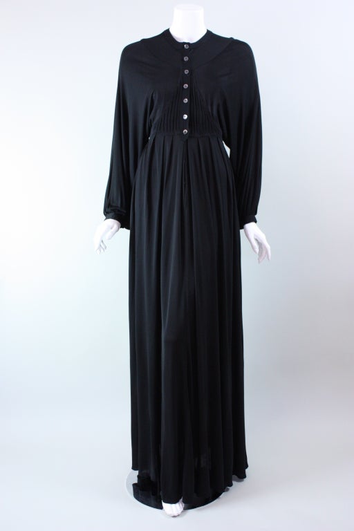 Statuesque gown from Jean Muir dates to the 1970's.  It is made out of black jersey crepe with minimal stretch.  Bodice has round neckline and is fitted throughout the ribcage where it has vertical pintucked details.  Extra wide batwing sleeves
