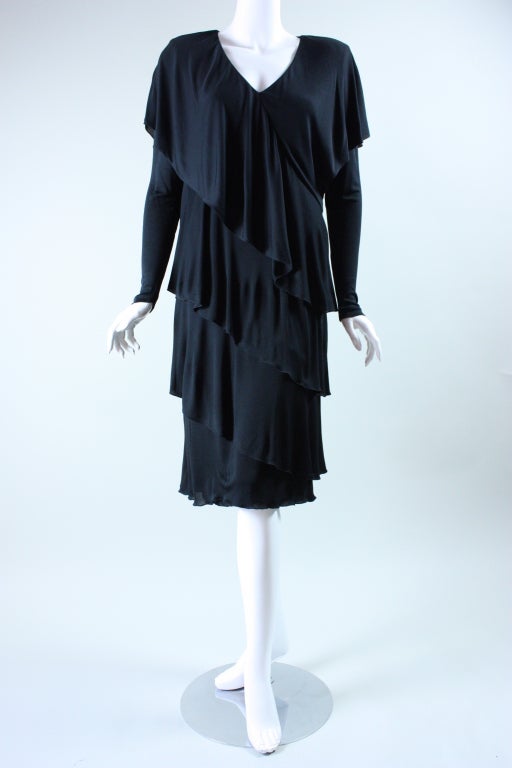 Late 1970's through early 1980's dress from Holly's Harp is made out of black matte stretch jersey.  It features four tiers that cascade diagonally across the body.  Long sleeves.  V-neck.  Lightly padded shoulders.  Lined except for in