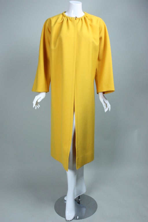 Classic overcoat from James Galanos circa 1970's through 1980's is made out of a bright yellow wool blend.   Round neck is gathered and has a center front squared gold-toned button.  Long sleeves are set into body at right angles.  Pockets are set