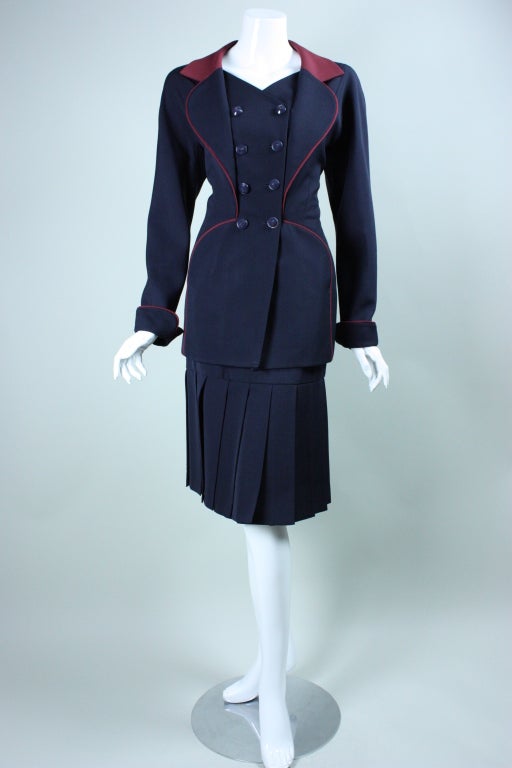 Fitted skirt suit from Karl Lagerfeld dates to the 1990's.  It is made out of navy wool gabardine with wine-colored accents.  Double-breasted jacket is highly segmented with vertical, curved seams.  Notch lapel.  Straight skirt has long carwash hem