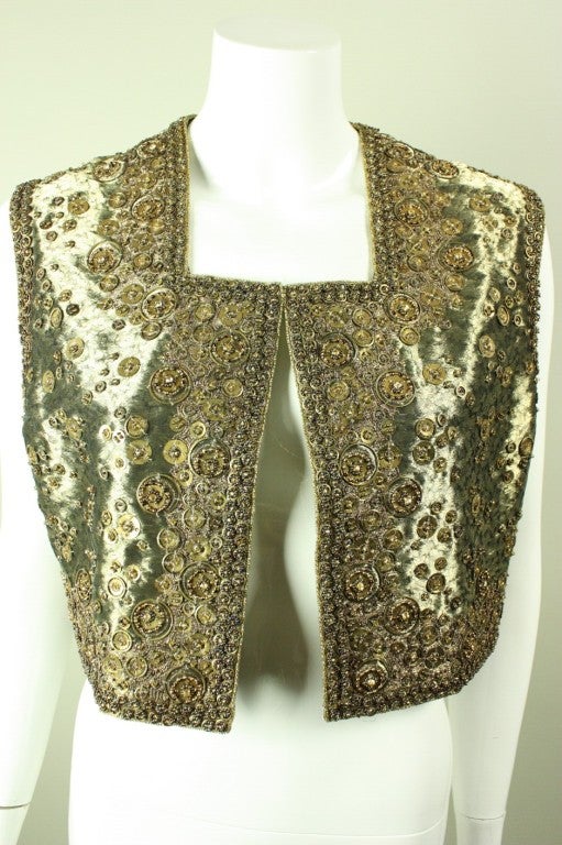 Gold vest from Joanna Mastroianni likely dates to post 2000.  It is all-over embellished with seed beads, metal discs, gold-toned pearls, and rhinestones.  Heavily embroidered in abstract pattern around edges.  Single center-front hook and eye