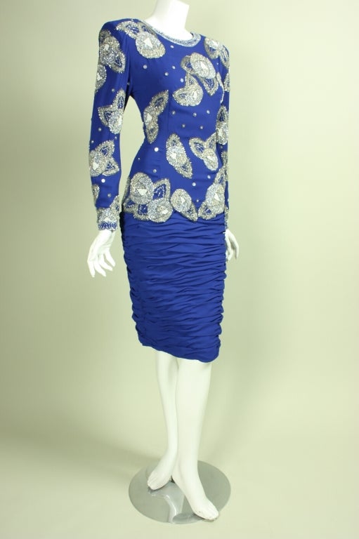 Cocktail dress from Fabrice dates to the 1980's through early 1990's.  It is made of blue fabric that features silver beadwork throughout front and back bodice and arms.  Skirt is fully ruched.  Center back zipper.  Lined.

Labeled size