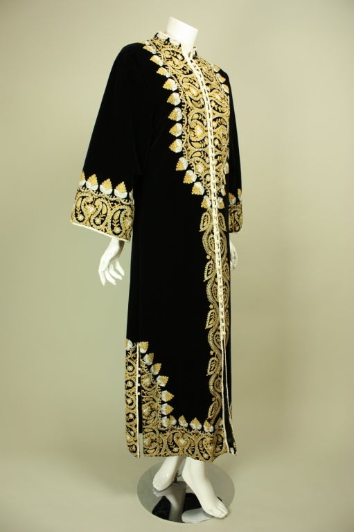 Heavily,embroidered caftan originated in Morocco and dates to the 1960's.  It is made of jet black velvet with yellow and white machine-embroidery down the center front, cuffs, hem, and at center back.  Mandarin collar.  Center front looped closures