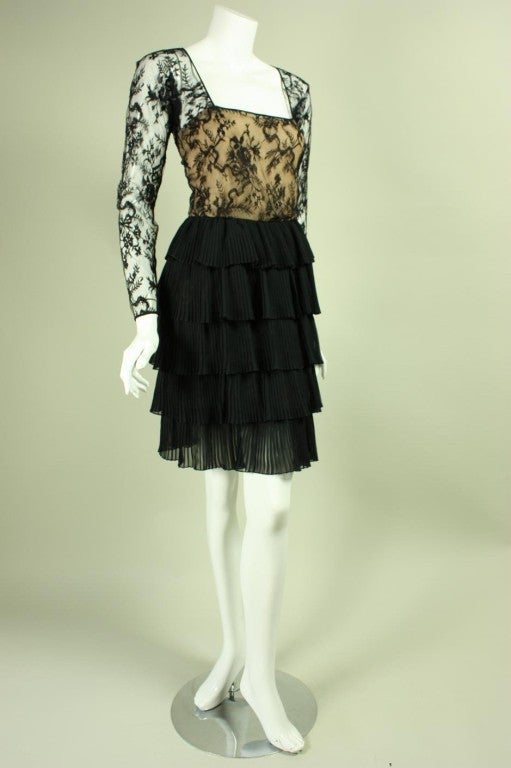 Lovely cocktail dress from Oscar de la Renta is made of black lace with a tiered pleated skirt.  Fitted bodice has squared scoop neck and long tapered sleeves with looped button closures at cuffs.  Knee-length skirt is made up of five tiers.  Lined